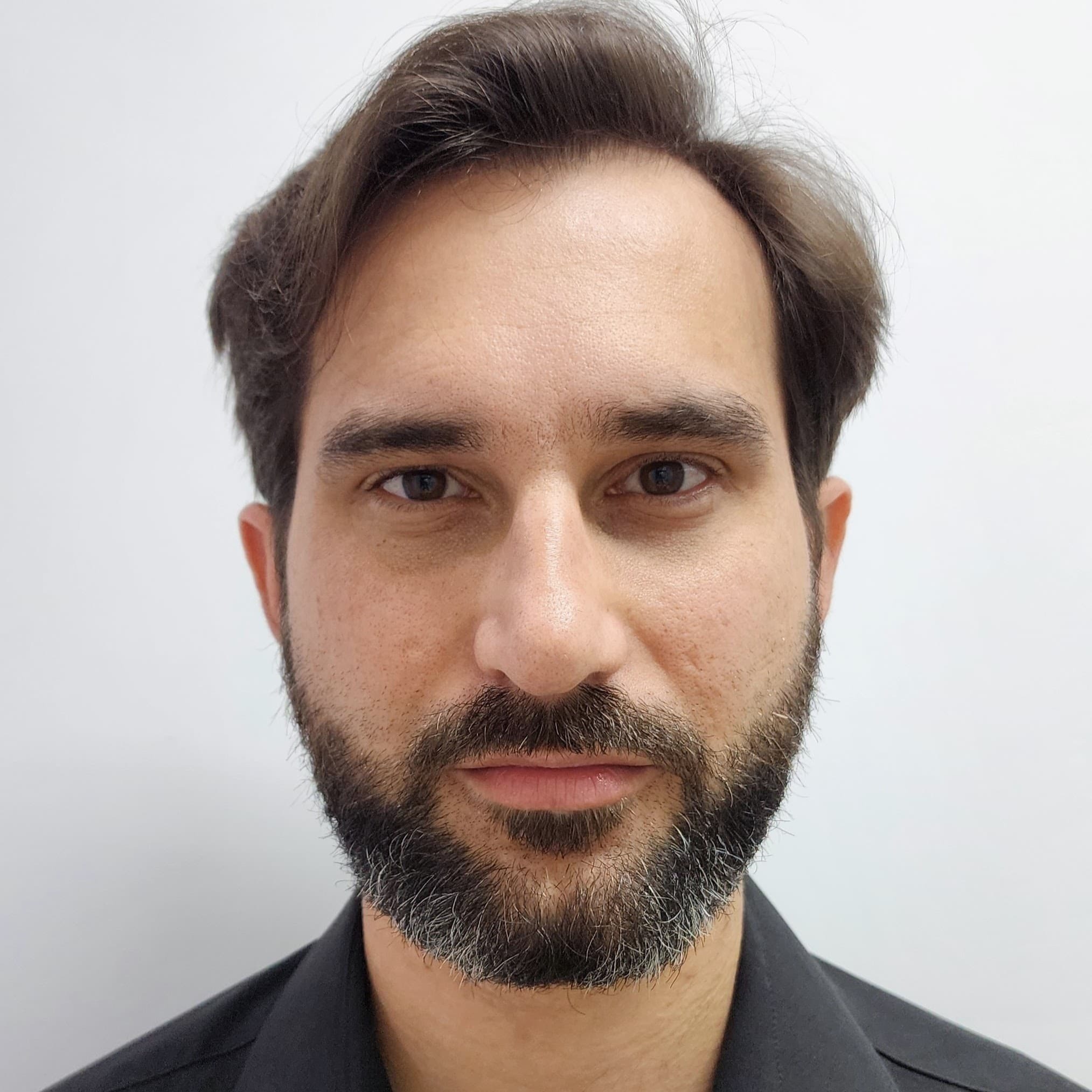 Foto de Rodrigo Klaic, com cabelos curtos e escuros, sorrindo e olhando diretamente para a câmera.